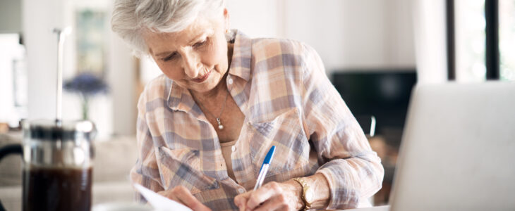 Shot of a happy senior woman flliing in paperwork while using her laptop at home