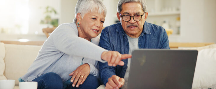 Senior, couple and pointing on laptop in living room with document for financial planning, investment or retirement. Elderly man, woman and technology for online banking, account balance or savings