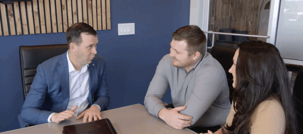 Man in a blue suit talking with a couple across the table in an office meeting.