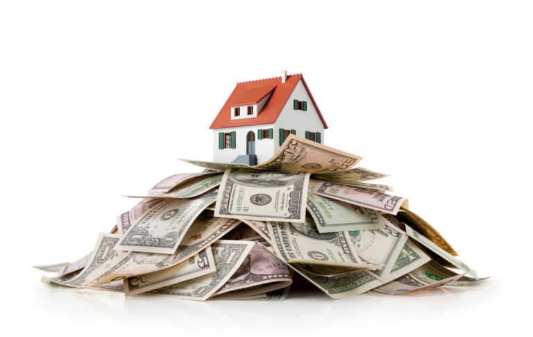 Miniature model house standing on a stack of dollar bills isolated on white background.