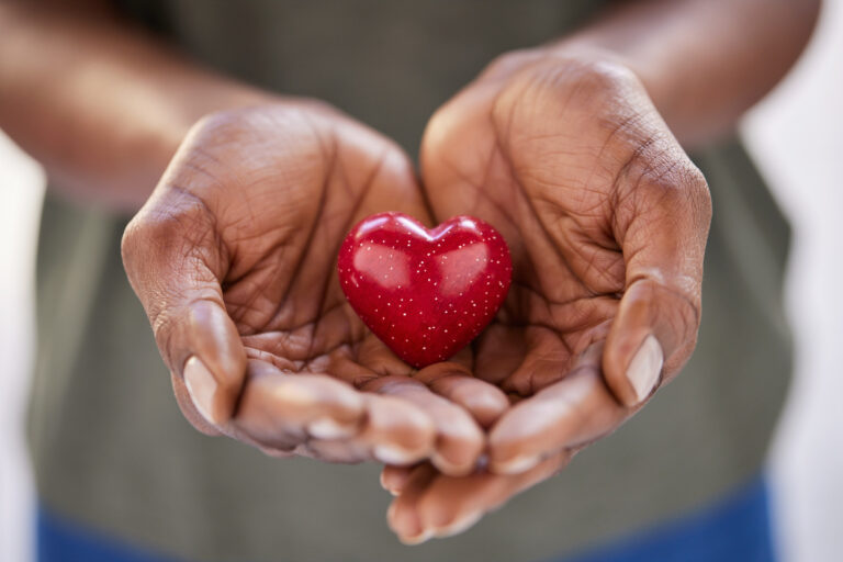 Close up of woman hands holding a small red heart. Small heart in the hands of a african woman. Solidarity, charity and responsibility concept.