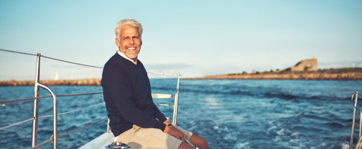 Smiling mature man sitting alone on the deck of his boat sailing along the coastline on a sunny afternoon