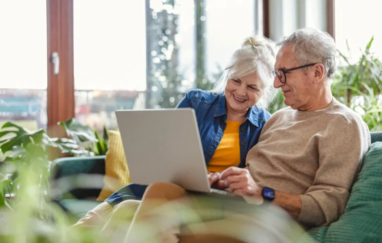 Senior couple using laptop while sitting on sofa in living room at home