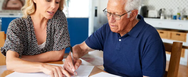Woman Helping Senior Man To Complete Last Will And Testament At Home