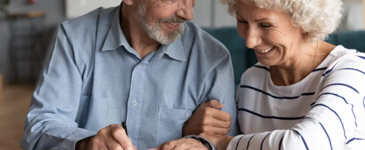 Happy senior older married couple discussing investing saving before signing paper agreement. Smiling middle aged man woman putting signature on marriage contract or making testate at lawyer office.